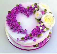 a heart shaped cake decorated with flowers on a white tablecloth and purple trimmings