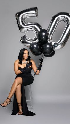 a woman sitting on a chair with balloons in the shape of numbers 50 and fifty