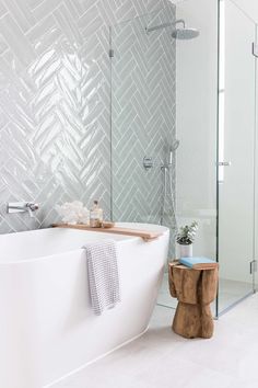 a white bath tub sitting next to a wooden stool in a bathroom under a shower