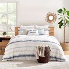 a white bed with blue and beige striped comforter in a bedroom next to a potted plant