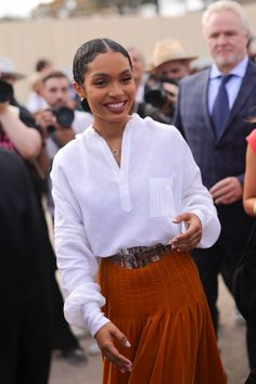 a woman in an orange skirt and white shirt smiles at the camera as people take pictures behind her