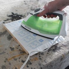 a person ironing something on top of a piece of paper with a green and white iron