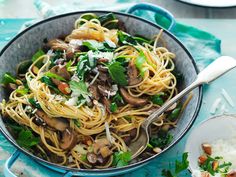 a pan filled with pasta and mushrooms on top of a blue table next to rice