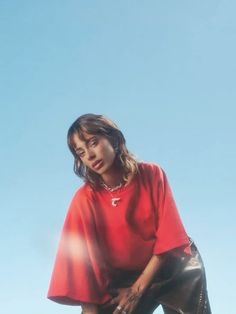 a woman in a red shirt and black leather pants posing for a photo with her hand on her hip