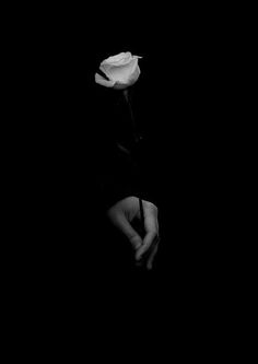 a black and white photo of a person holding a rose in their hand with the dark background