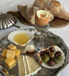 an assortment of cheeses, olives and bread on a silver tray