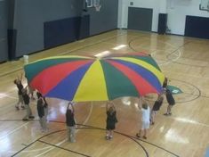 a group of people standing on top of a basketball court holding up a large umbrella