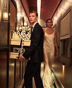 a man and woman are walking down the hallway in formal attire with boxes on their backs