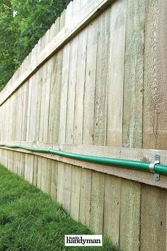 a green hose attached to the side of a wooden fence with grass in front of it