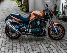 an orange and black motorcycle is parked on the brick road next to a garage area