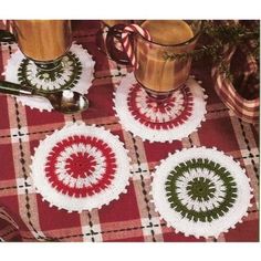 three crocheted coasters sitting on top of a table next to two cups