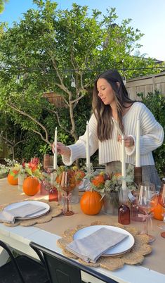 a woman setting a table with candles and pumpkins