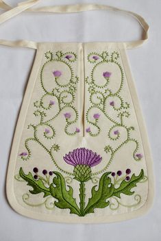 an embroidered bag with purple flowers and green leaves on the front, hanging from a white ribbon