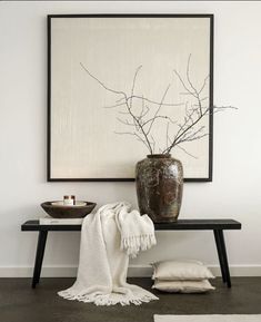 a vase sitting on top of a wooden table next to a white blanket and pillow