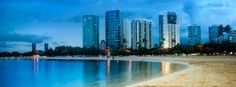 a beach with buildings in the background and water on the sand near it at night