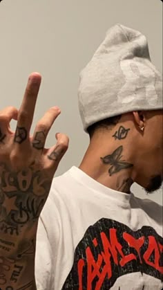 a man with tattoos making the v sign while wearing a t - shirt and hat