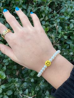 a woman's hand wearing a yellow smiley face beaded bracelet and matching ring