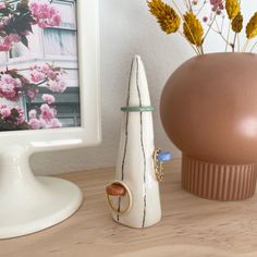 a vase with flowers in it next to a ring holder on a wooden table near a framed photograph