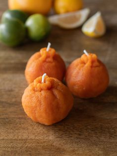 three orange candies sitting on top of a wooden table next to lemons and limes