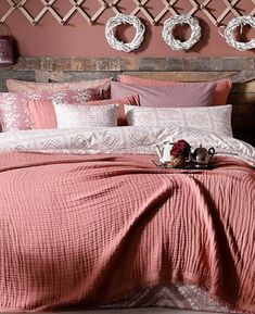 a bed with pink sheets and pillows in a bedroom next to two wreaths on the wall