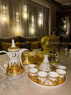 a table topped with gold and white dishes next to a tea pot filled with cups