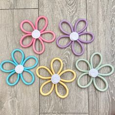 four different colored flower shaped hair clips on a wooden floor with one being held in the other's hand