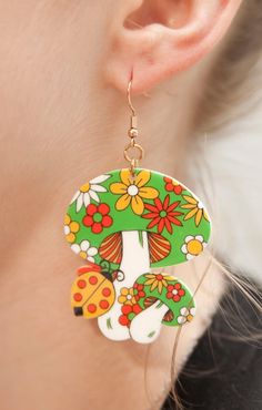 Get ready to embrace the spirit of the 70s with these Green and Groovy Flower Mushroom Bunch Earrings. Inspired by the retro vibes of the era, these earrings feature a delightful bunch of mushrooms filled with flowers and in vibrant colors. Crafted from lightweight acrylic and adorned with gold-coated stainless steel hooks, these earrings offer a perfect blend of comfort, style, and nostalgia. Product Details: Size: Each earring measures approximately 2 3/4 inches from the top of the hook to the Retro Spring Flower Earrings Gift, Spring Retro Flower Earrings Gift, Vintage Flower Earrings For Summer, Vintage Summer Flower Earrings, Retro Multicolor Flower Earrings For Gift, Whimsical Green Mushroom Design Earrings, Whimsical Green Mushroom Earrings, Toothpaste Kisses, Groovy Fashion