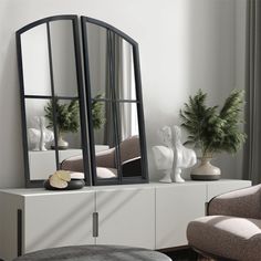 a mirror sitting on top of a white dresser next to a chair and potted plant