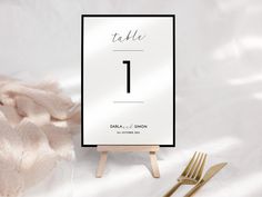 a table number card sitting on top of a wooden easel next to a fork