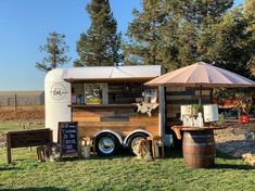 a food truck parked in the grass with an umbrella over it's head and two barrels next to it