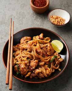 a bowl filled with noodles and meat next to chopsticks on a table top