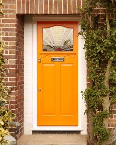 an orange front door on a brick building with potted plants and trees around it