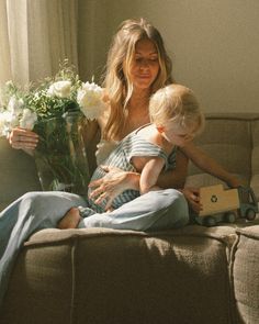 a woman sitting on a couch with a child and flowers in front of her,