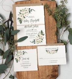 the wedding stationery is laid out on a cutting board with greenery and flowers