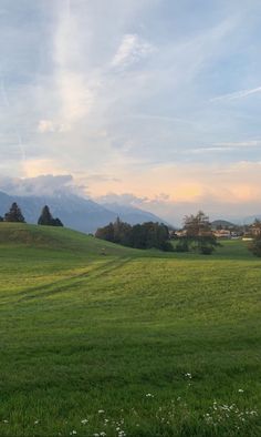 a green field with mountains in the background and clouds in the sky above it at sunset