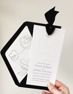 a person holding up a black and white wedding card