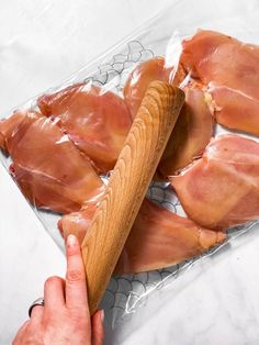 a person holding a wooden stick over bacon wrapped in plastic