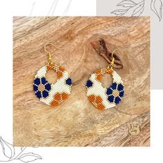 the beaded hoop earrings are decorated with an orange, white and blue cross stitch pattern