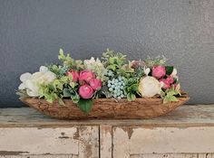 a wooden bowl filled with flowers on top of a table next to a gray wall