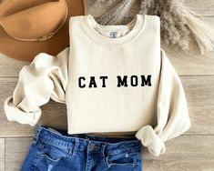 Celebrate the ultimate Cat Mom in your life with our personalized "Cat Mom" sweatshirt! This cozy and stylish sweatshirt is the purrfect gift for Mother's Day, birthdays, or any occasion where you want to show appreciation to a dedicated cat parent. Crafted with comfort in mind, this sweatshirt features a charming "Cat Mom" print on the front, declaring her love for her feline friend. As an extra touch, the sleeve is adorned with her beloved cat's name, making it a truly unique and heartfelt gif Cat Mom Mothers Day, Cat Mom Sweater, Cat Mom Sweatshirt, Leave Us A Review, Class Outfit, Cat Mama, Cat Christmas Gift, Mom Sweater, Mom Cat