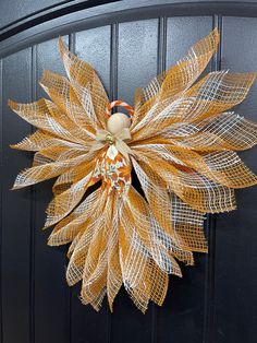 an orange and white mesh wreath hanging on a black door with a burlock