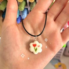 a hand holding a small white and red flower charm on it's left wrist