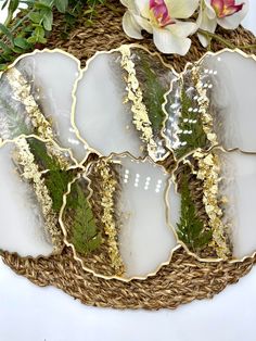 four white and gold plates sitting on top of a wicker basket next to flowers