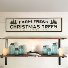 a shelf with jars and candles on it in front of a sign that says farm fresh christmas trees