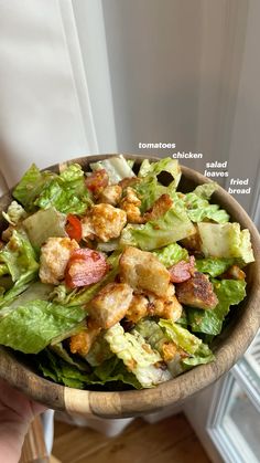 a wooden bowl filled with lettuce, bacon and tomato salad on top of a window sill