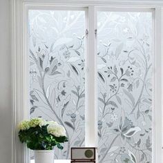 a vase with flowers sitting next to a window on a table in front of it