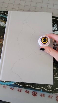 a hand holding a fake eyeball on top of a white sheet of paper next to a ruler