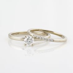 two gold wedding rings with diamonds on top and one diamond in the middle, against a white background