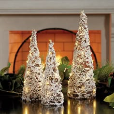 three lighted trees sitting on top of a table next to a fire place in front of a fireplace