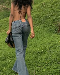 a woman walking in the grass with her back turned to the camera and wearing high waist jeans